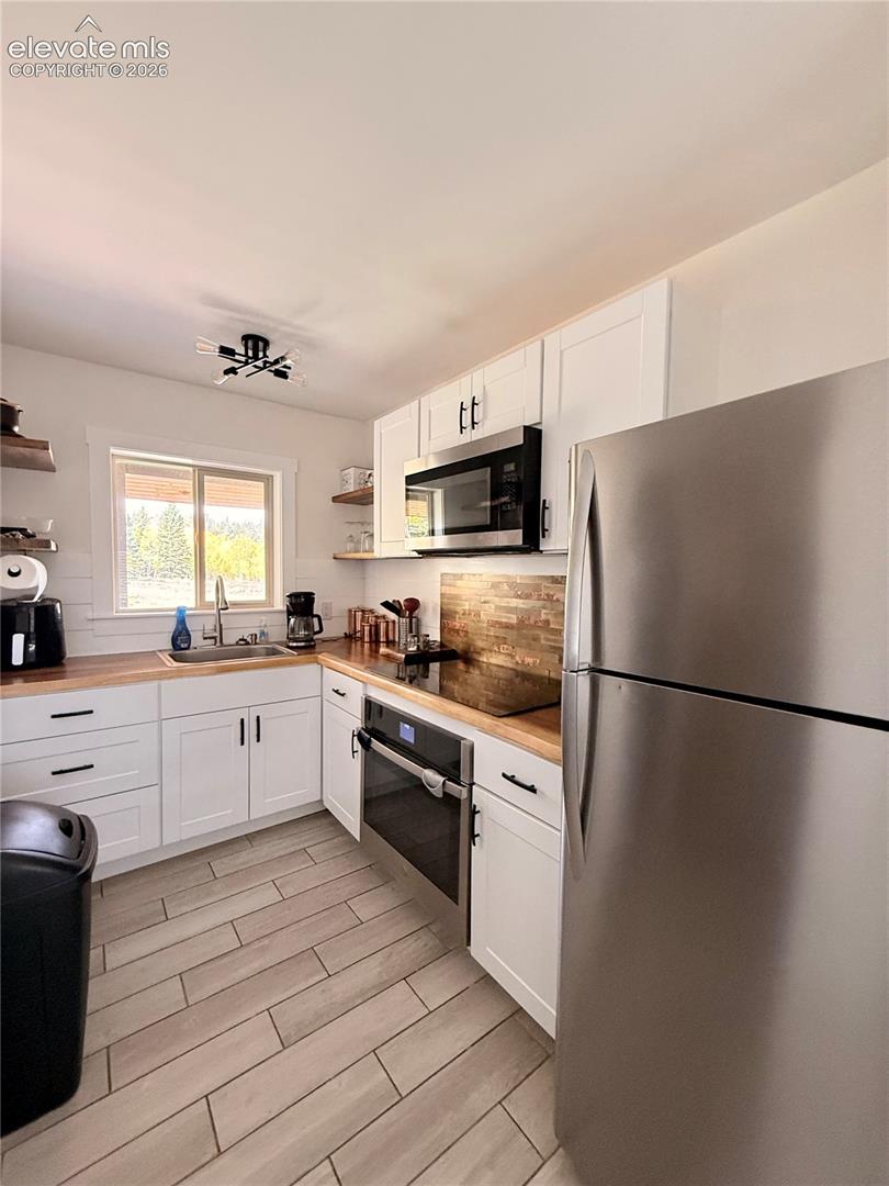 White shaker cabinetry with black hardware, wood-finish countertops, stainless steel appliances, tile flooring, and a window above the sink