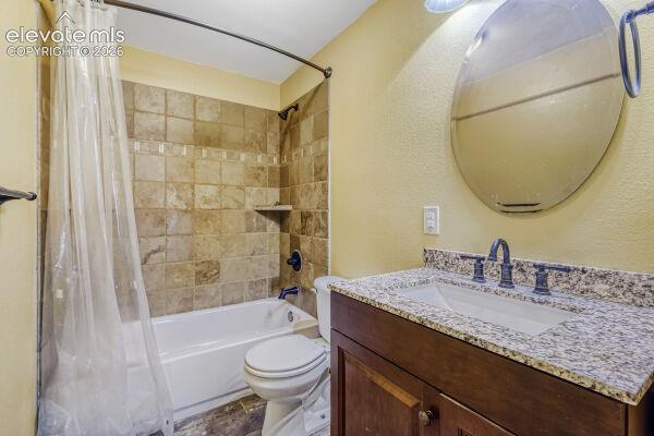 Bathroom featuring a tub/shower combination with tile surround, a dark wood-finish vanity with a granite-style countertop, an undermount sink, and a circular mirror