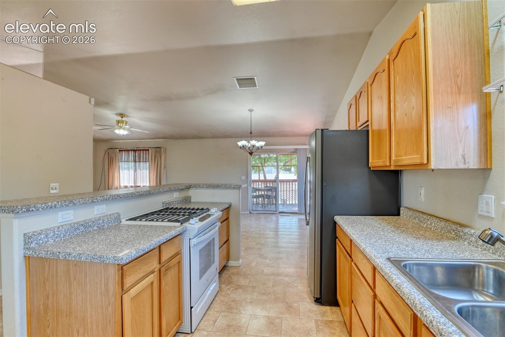 Kitchen featuring wood cabinetry, stone-finish laminate countertops, a stainless steel double-basin sink, a built-in gas cooktop, and tile flooring