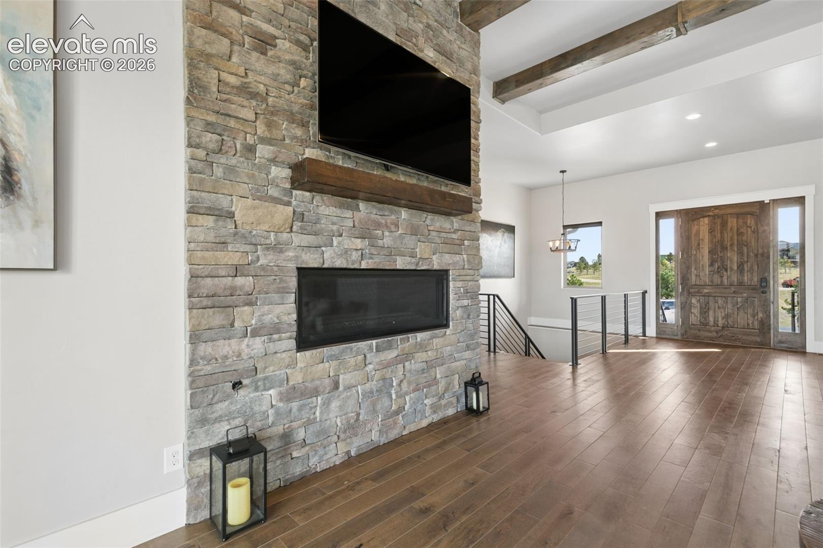 Stone-clad fireplace with wood mantle, wood-finish flooring, exposed ceiling beams, and a substantial wood entry door with side windows