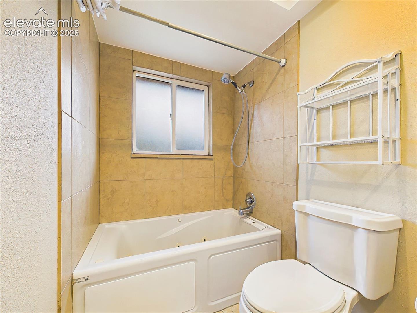 Tiled tub and shower surround with built-in shelving and a frosted window for added natural light and privacy.