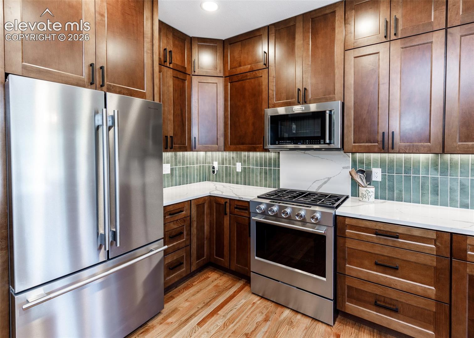 Stainless steel appliances, wood-finish flooring, white countertops, tile backsplash, and wood cabinetry