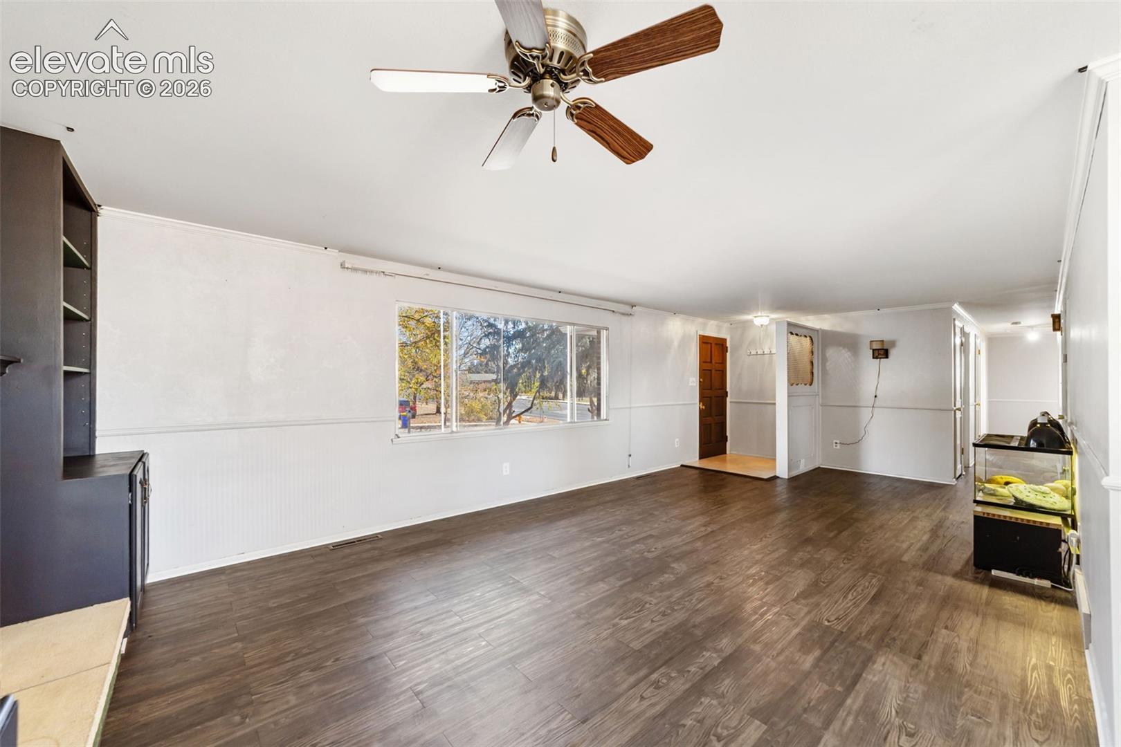 Spacious interior featuring dark wood-finish flooring, a ceiling fan with integrated lighting, and multiple windows