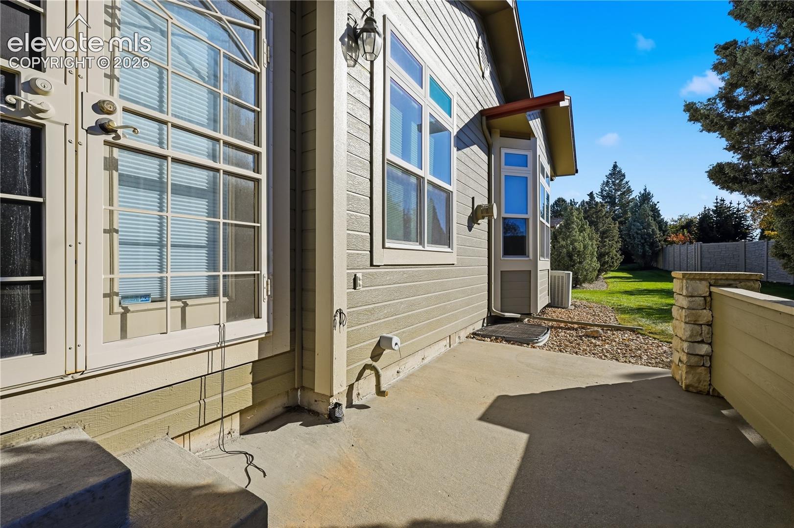 Concrete patio featuring lap siding, dual French doors with sidelights, bay window, and stone-accented perimeter wall