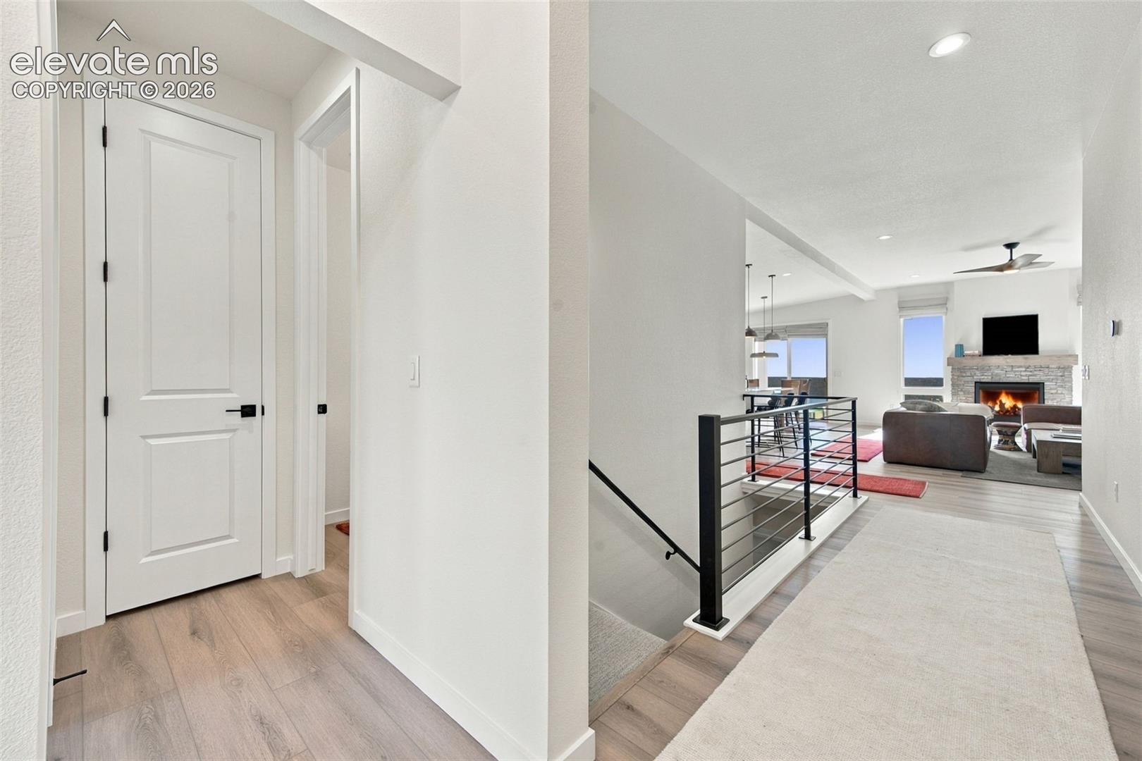 Interior featuring wood-finish flooring, staircase with a black metal railing, recessed ceiling lighting, and a stone-surround fireplace