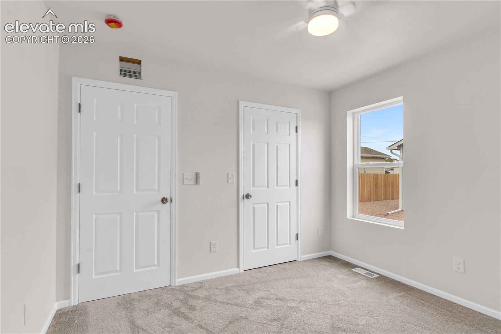Neutral-toned carpeted flooring, two six-panel interior doors, and a ceiling-mounted light fixture