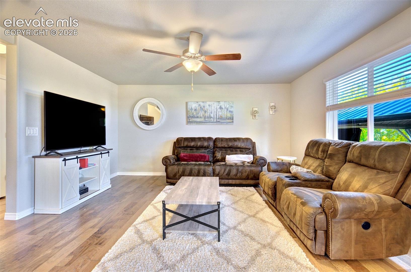 Living area featuring wood-finish flooring, a neutral color palette, a ceiling fan with integrated lighting, and horizontal window blinds