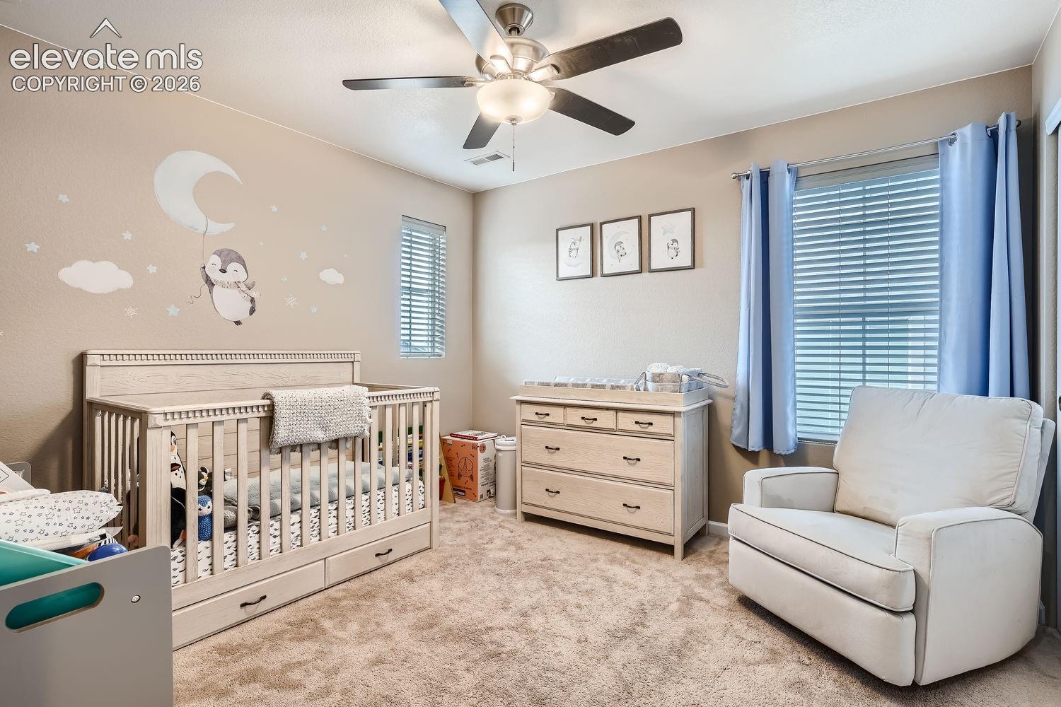 Neutral-toned room featuring plush wall-to-wall carpeting, a multi-blade ceiling fan with integrated lighting, dual windows with horizontal blinds, and textured walls