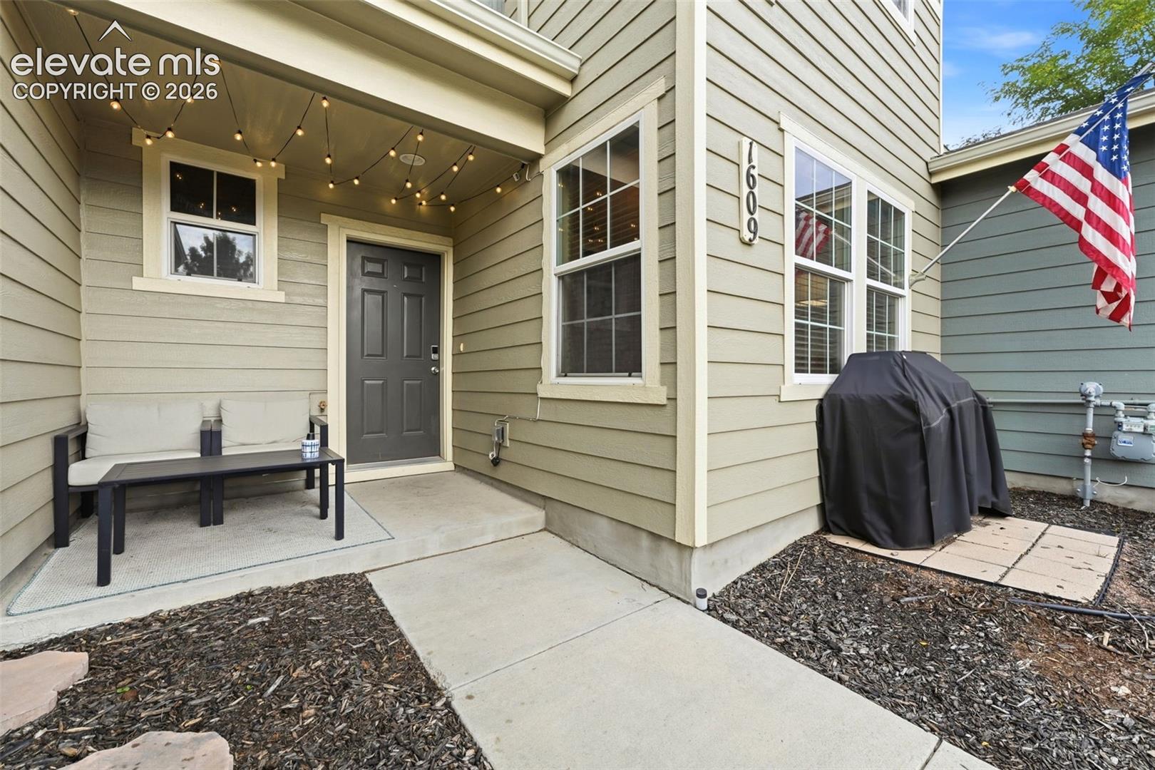 Covered entry with concrete patio, dark gray entry door, and light green horizontal siding