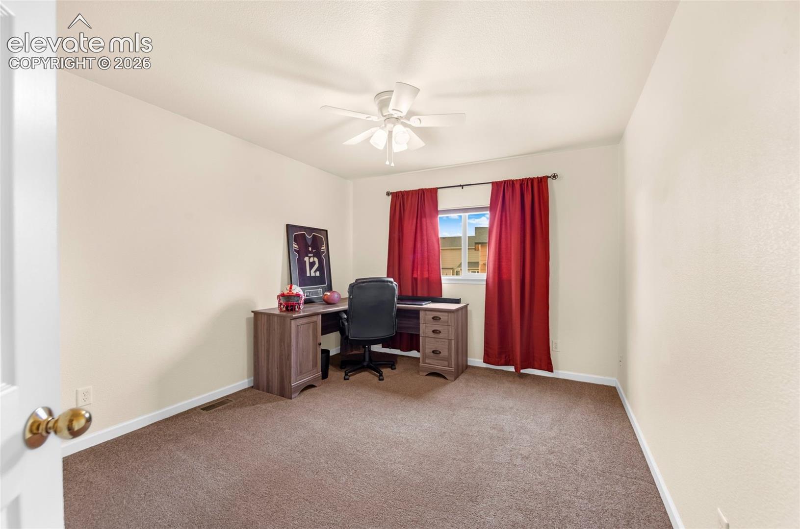 Bright room featuring a window with red drapery, light-colored walls, and brown carpeting