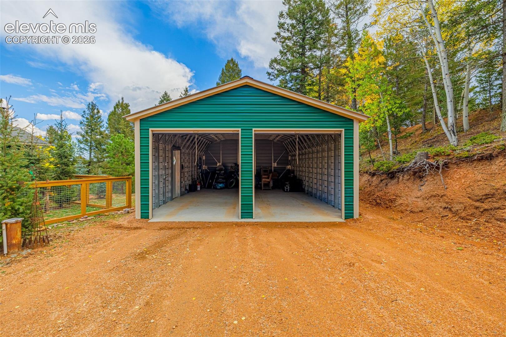 Detached two-car metal garage featuring a green corrugated exterior, two wide entry bays, and concrete flooring