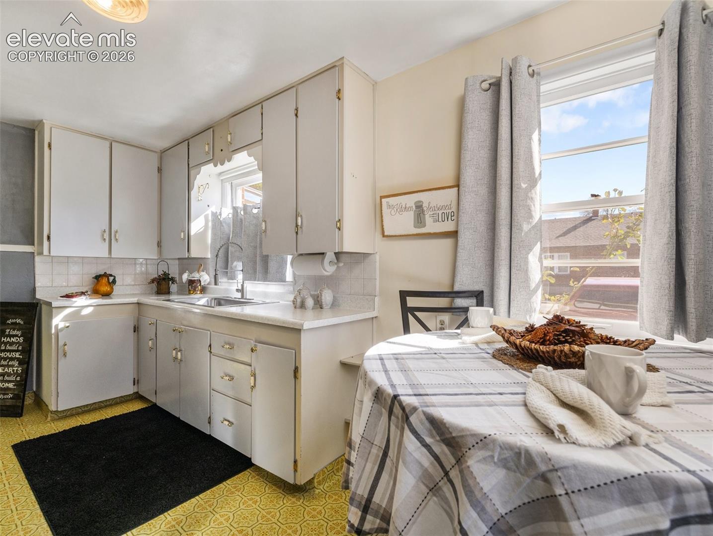 Kitchen featuring cabinetry with polished hardware, stainless steel sink with a high-arch faucet, patterned flooring, and large window