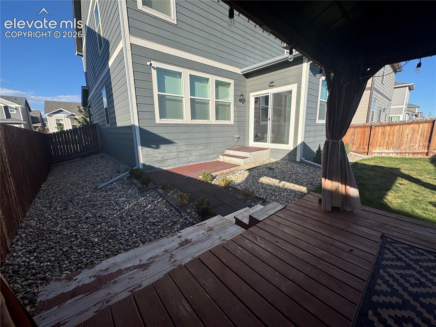 Exterior rear elevation featuring horizontal lap siding, a raised wood deck, stone ground cover, and a sliding glass door