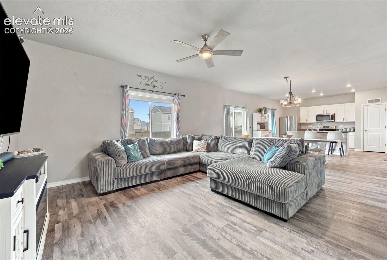Wood-finish flooring, ceiling fan with integrated lighting, kitchen featuring white cabinetry, and multi-light chandelier fixture
