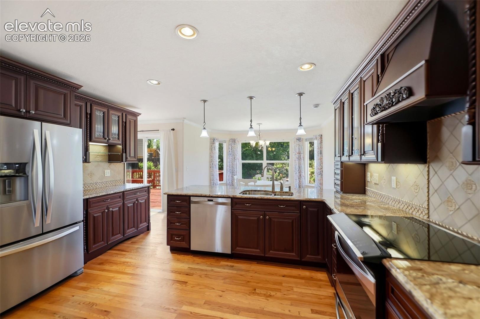Kitchen featuring wood-finish flooring, dark wood cabinetry, stainless steel appliances, and granite countertops