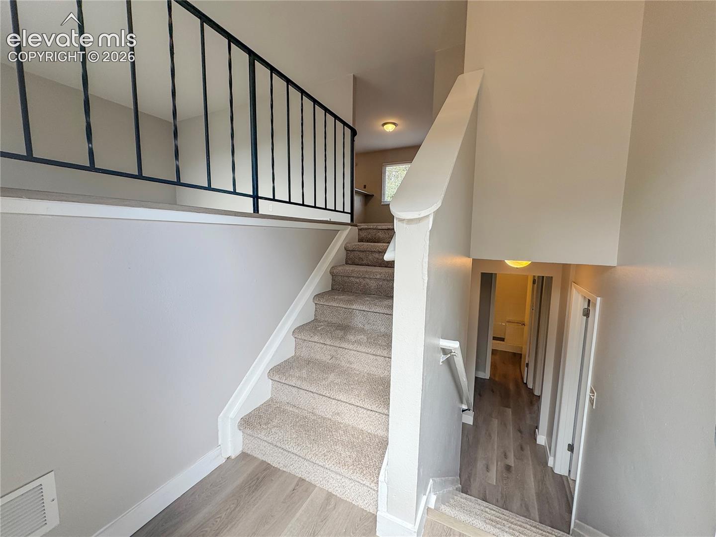 Staircase featuring carpeted treads, metal balustrades, wood-finish flooring, and wall-mounted handrails