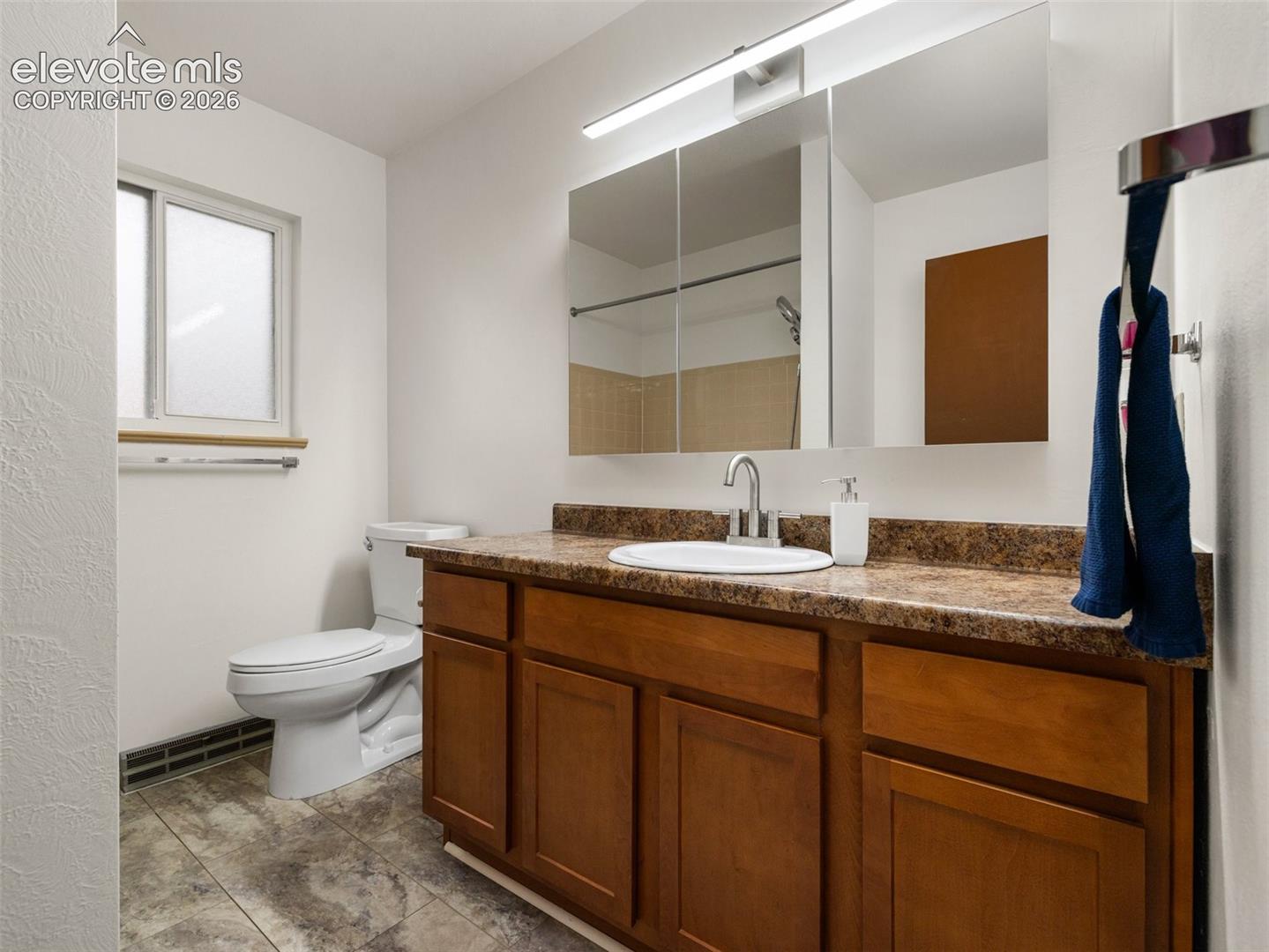 Single vanity with wood-finish cabinetry, integrated sink, and composite countertop