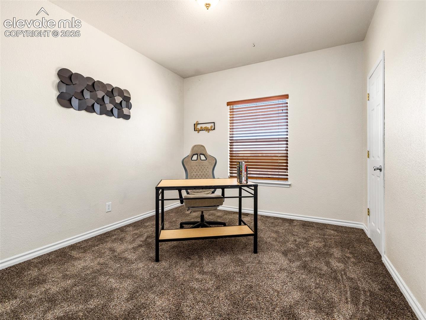 Textured wall finish, brown carpeting, window with wood-toned blinds, white baseboards