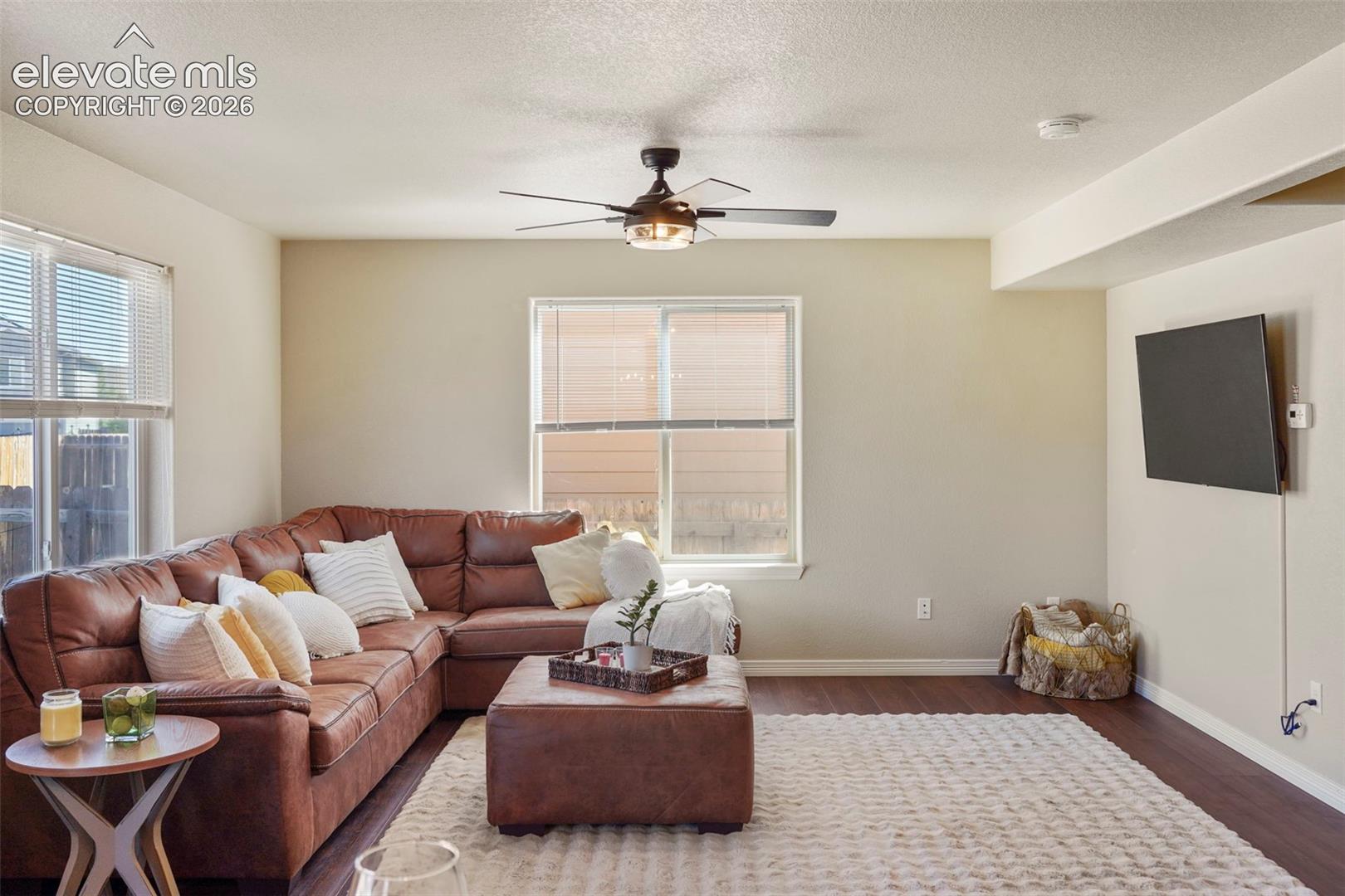 Living area featuring wood-finish flooring, a ceiling fan with integrated lighting, and multiple windows