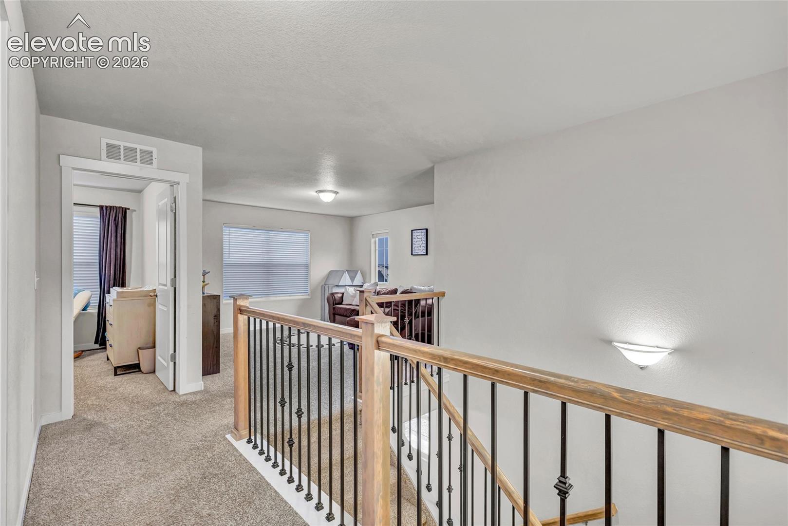 Carpeted landing with white walls, wood-finish handrails, and black metal balusters
