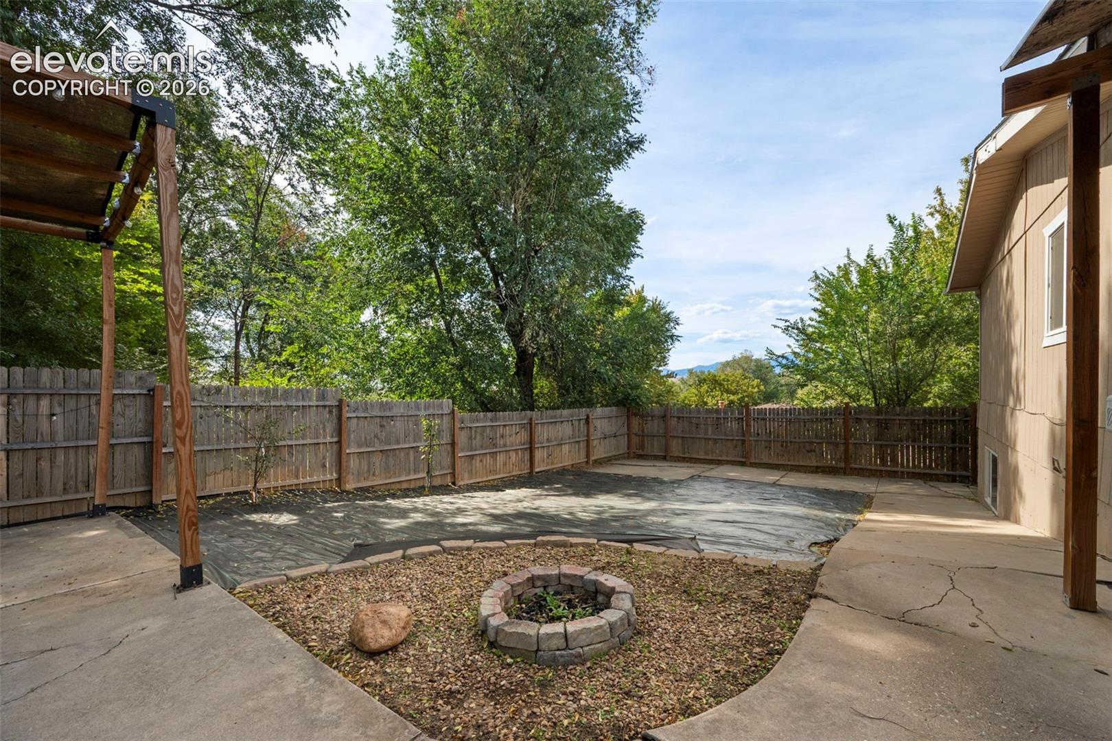 Backyard featuring a concrete patio, stone-bordered fire pit, wood-post pergola, and perimeter wood fencing