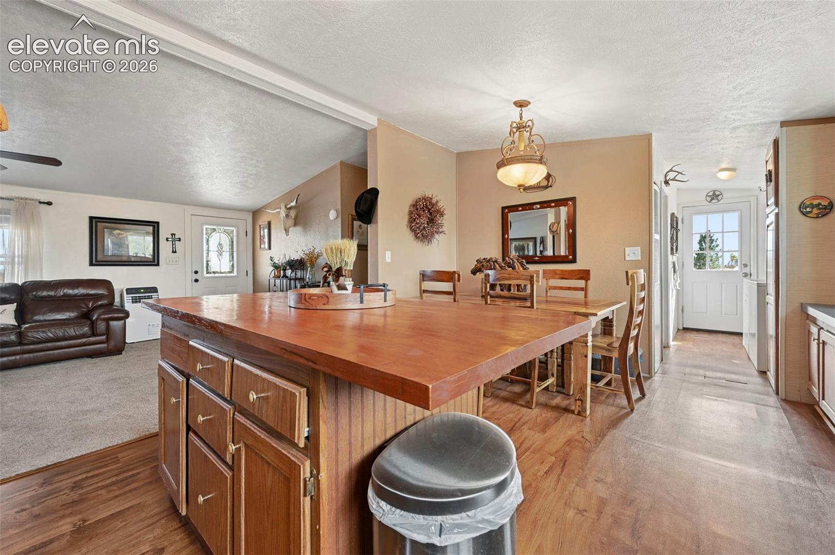 Kitchen island featuring a wood-surface countertop and stained wood cabinetry, accented by a decorative hanging light fixture, wood-finish flooring, and two exterior doors with glass pane inserts