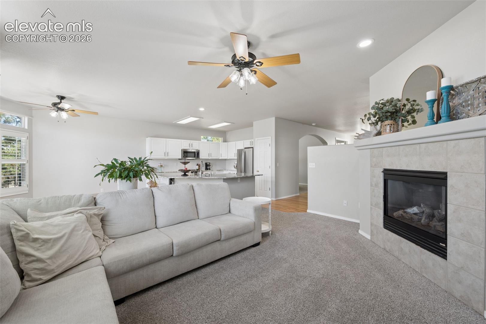 Open-concept interior featuring a fireplace with stone-finish surround, ceiling fans with integrated lighting, recessed lighting, and kitchen cabinetry