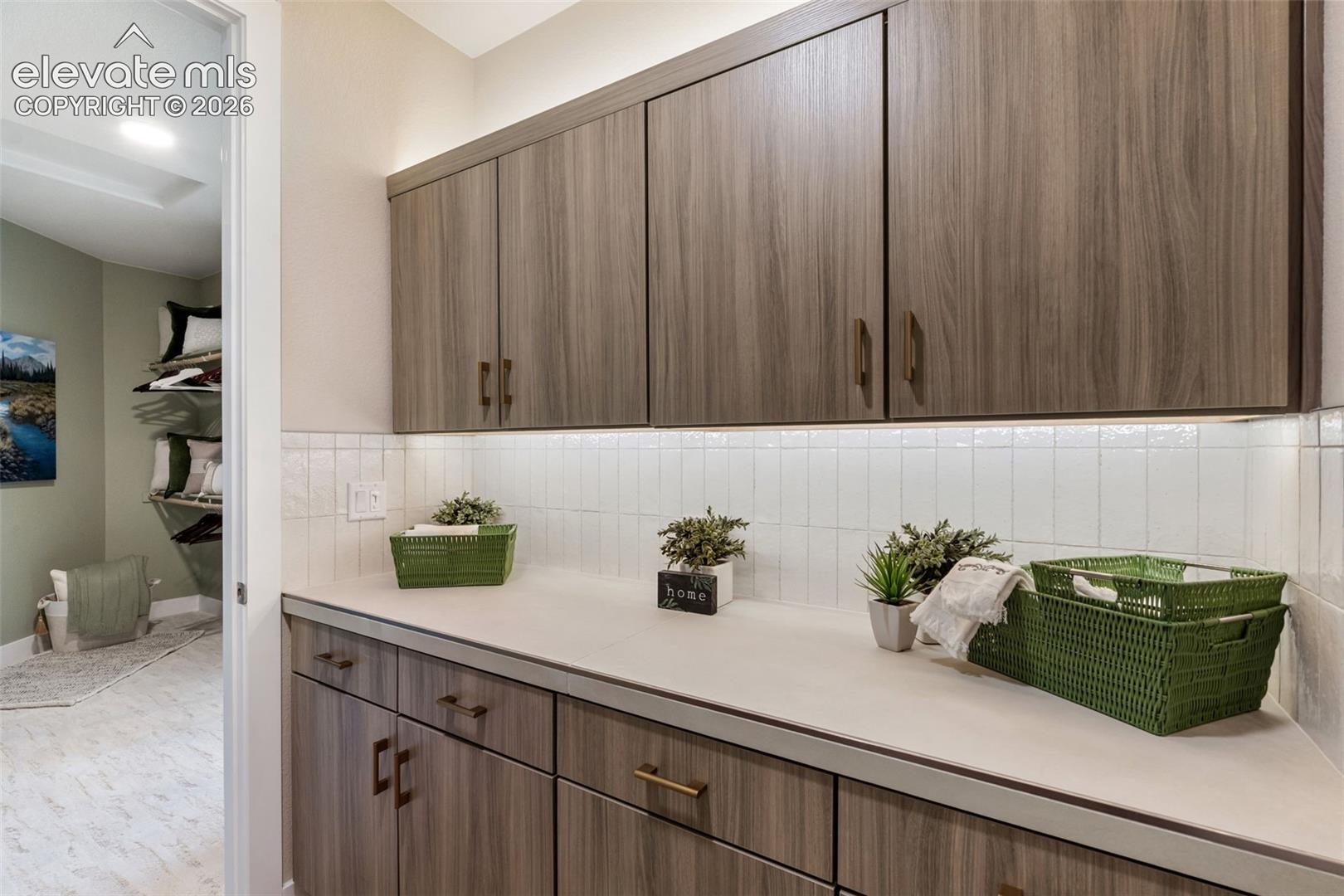 Wood-finish cabinetry with metallic hardware, solid surface countertops, and white vertical tile backsplash