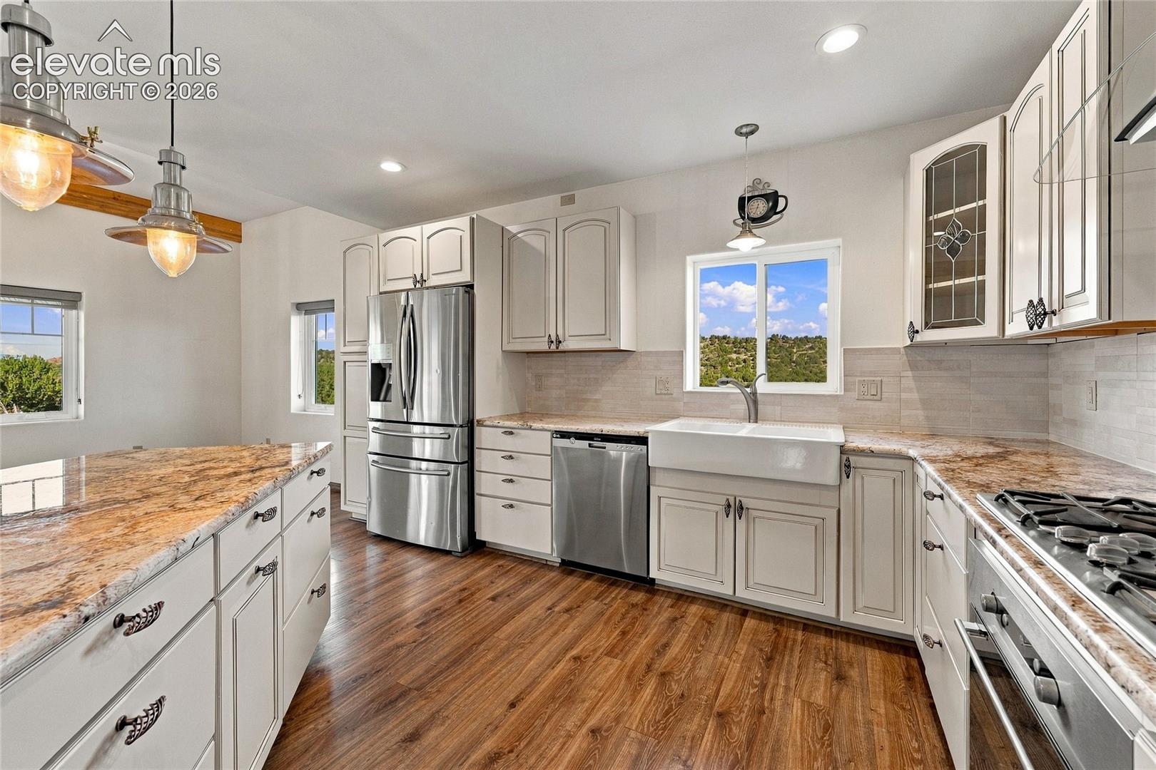 Kitchen featuring white cabinetry, stone-finish countertops, apron-front sink, stainless steel appliances, and wood-finish flooring