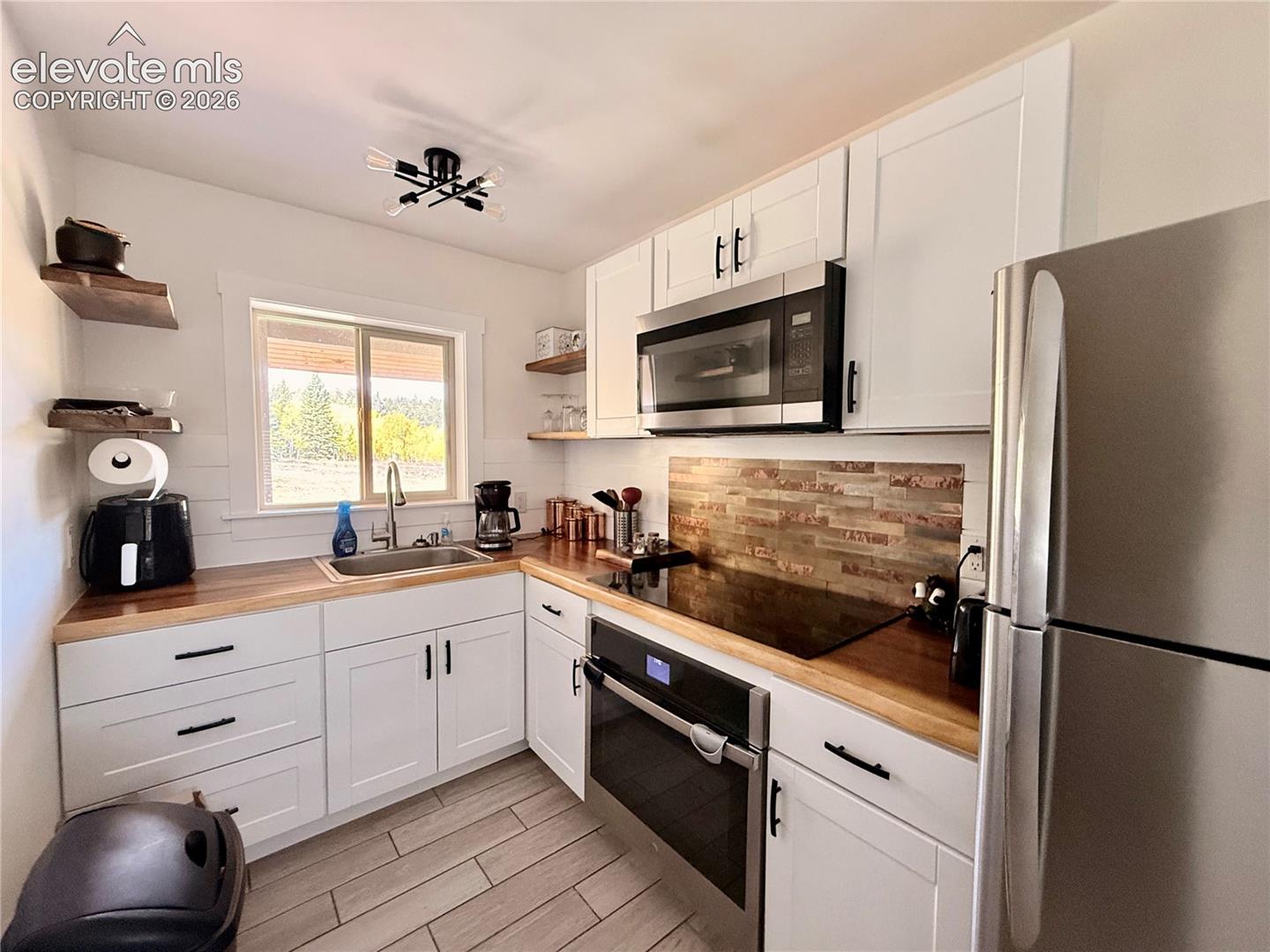White cabinetry with matte black hardware, wood-finish countertops, stainless steel appliances, a tile backsplash, and light-toned flooring