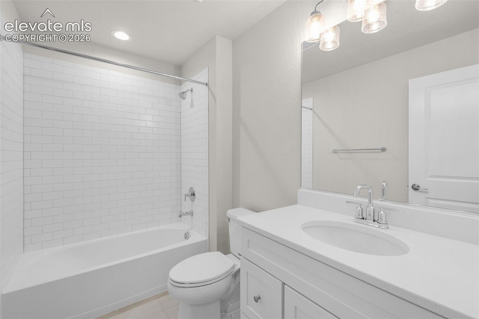 Bathroom featuring a white vanity with a composite countertop, an oval undermount sink, a large wall-mounted mirror, and a tub-shower combination with white subway tile surround
