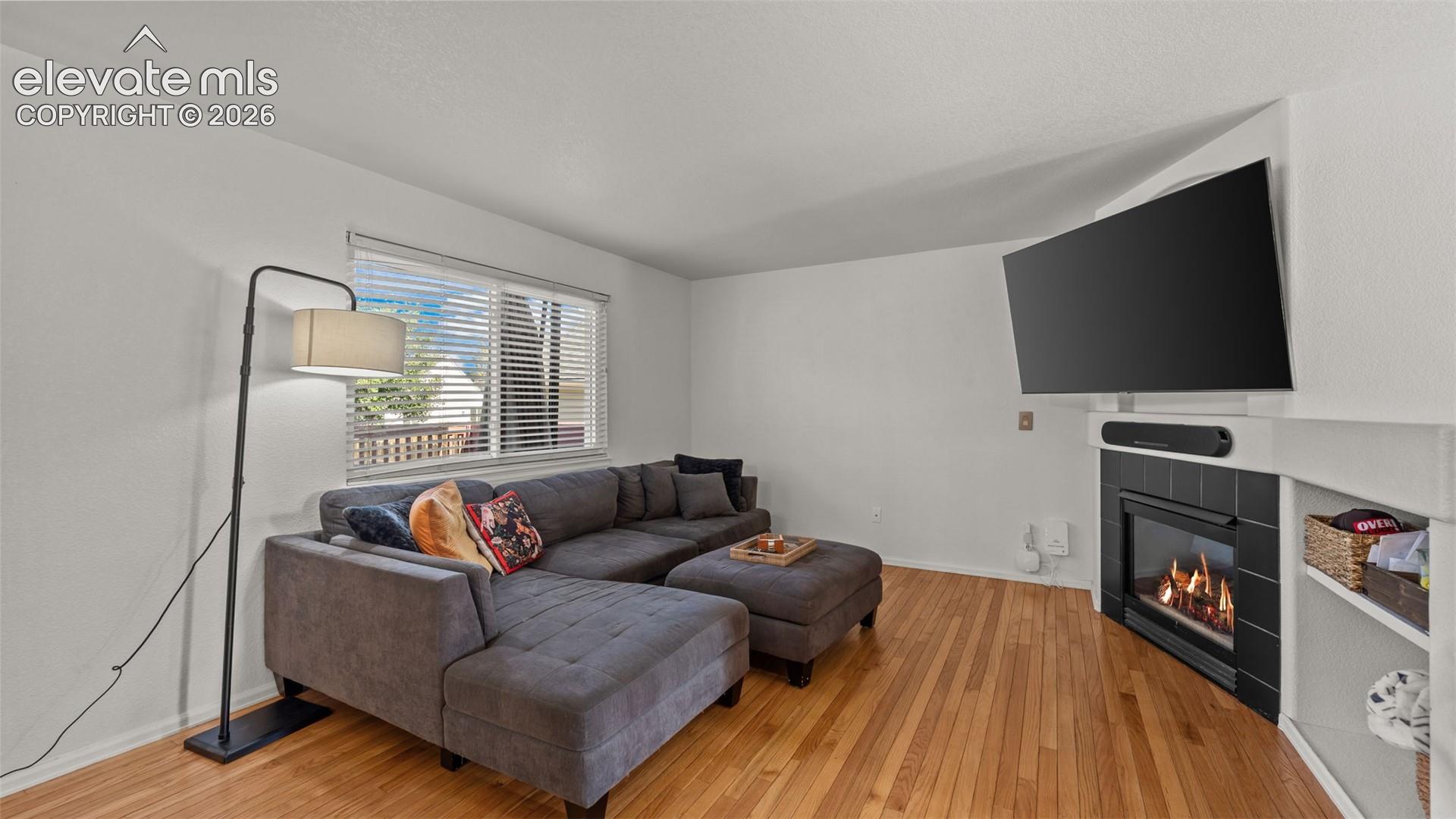Hardwood-style flooring, a large window with blinds, a corner fireplace with black tile surround, and built-in shelving