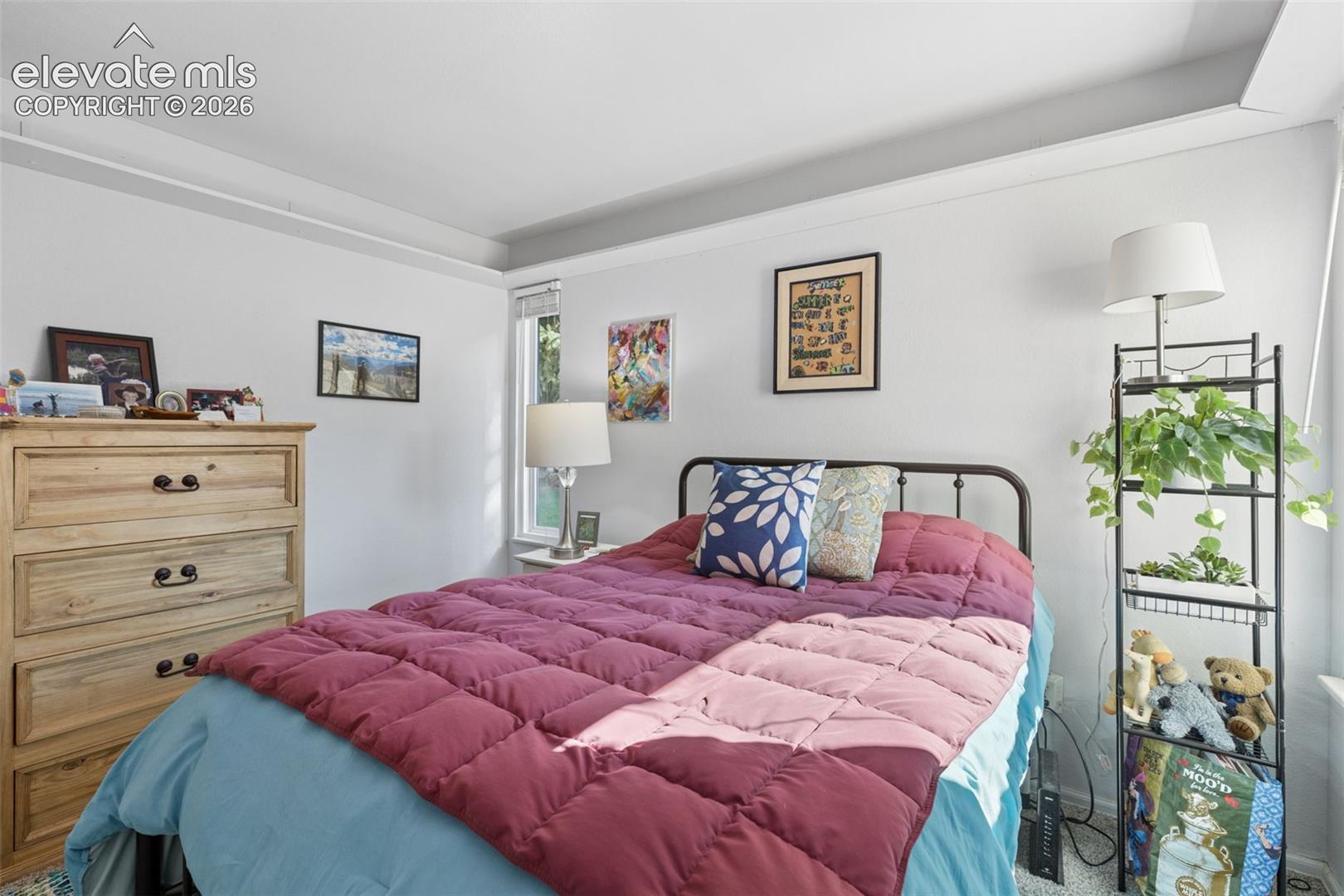 Recessed ceiling feature, natural light from a window, built-in shelving, wood-finish dresser with dark hardware, and a dark metal bed frame