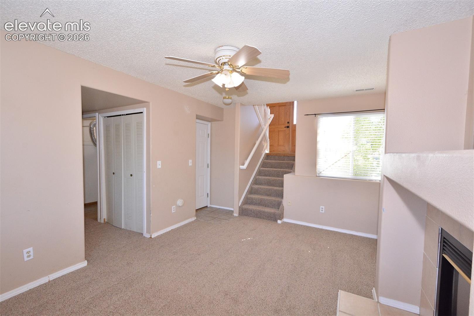 Carpeted living space with a ceiling fan, a window with blinds, and a built-in fireplace