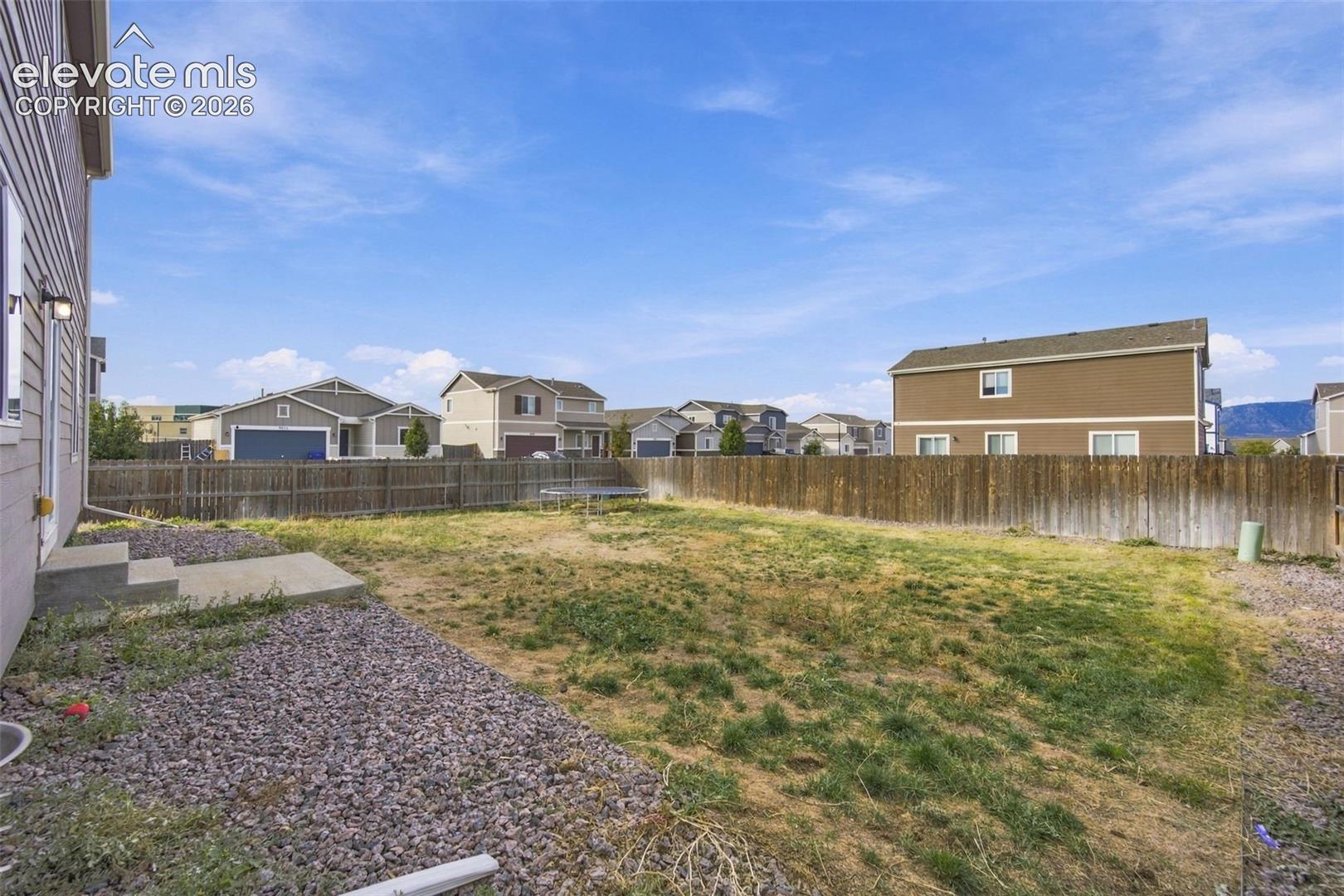 Fenced backyard featuring an expansive lawn, gravel ground cover, and a concrete patio