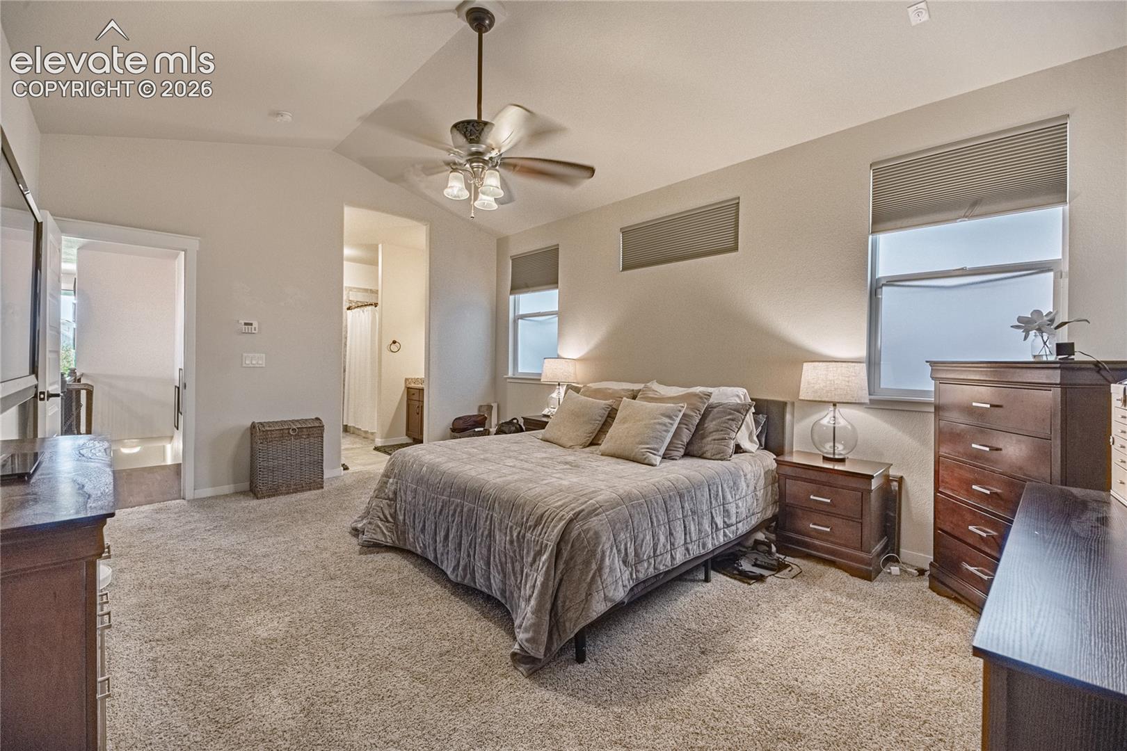 Vaulted ceiling featuring a central multi-blade ceiling fan with integrated lighting, neutral wall-to-wall carpeting, and transom-style windows