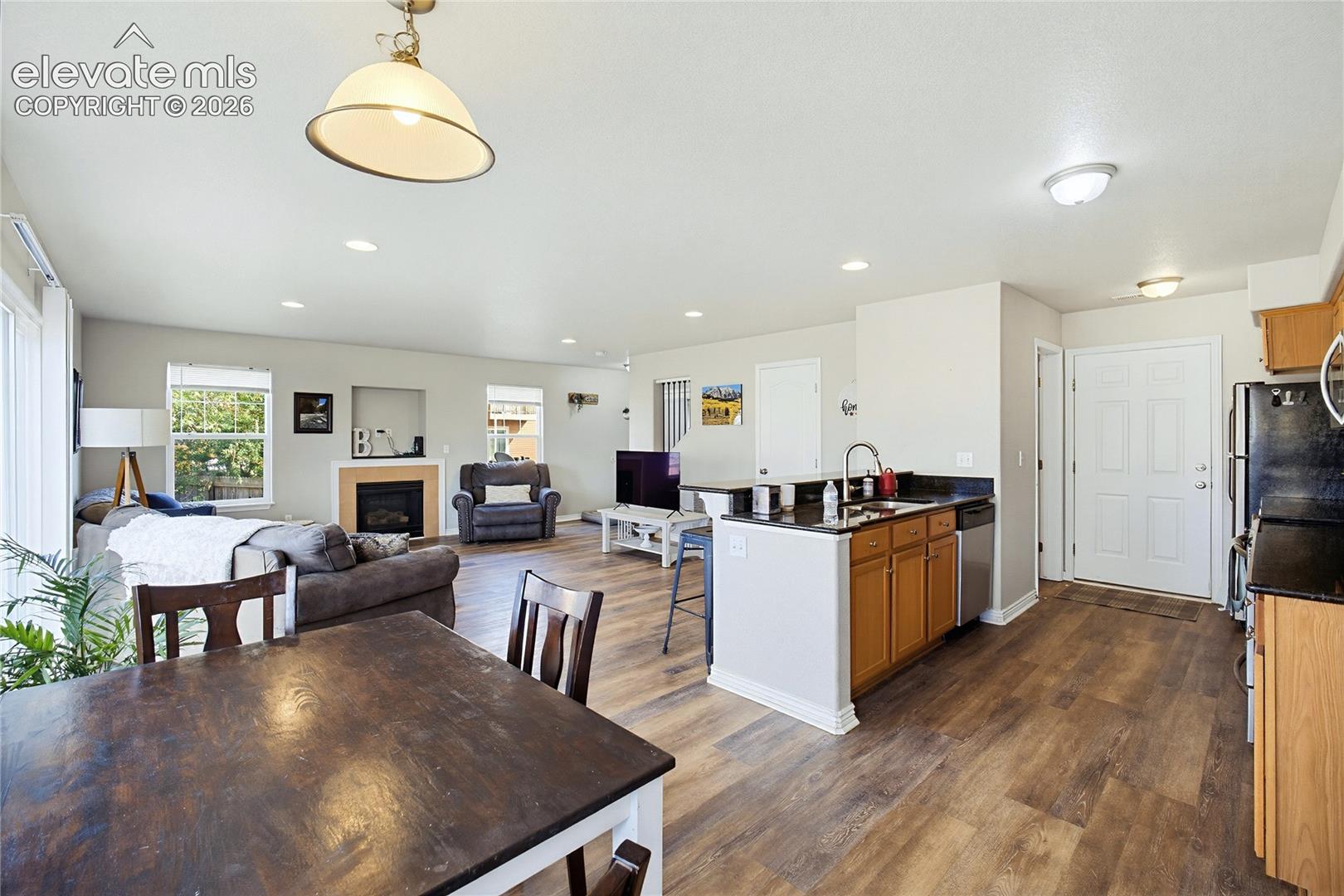 Open-concept floor plan featuring wood-finish flooring, a kitchen island with dark countertops, recessed lighting, and a built-in fireplace