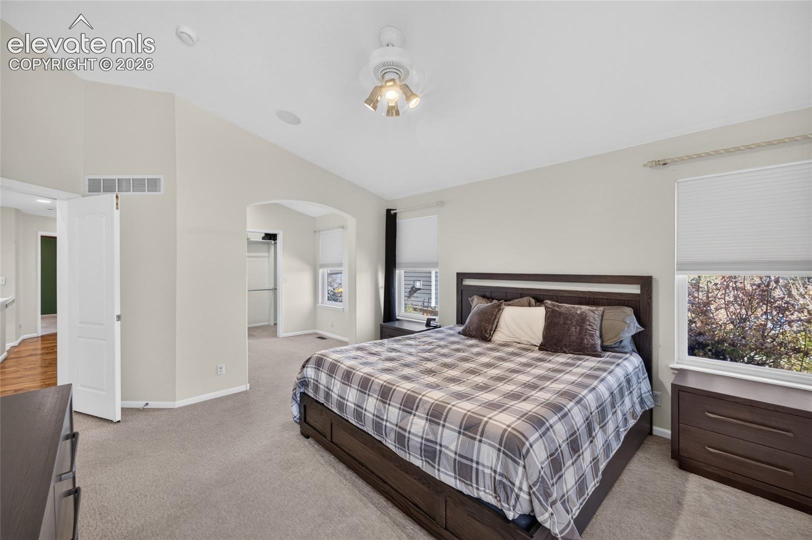 Vaulted ceilings, neutral wall tones, arched wall opening, recessed lighting, and large windows with integrated blinds