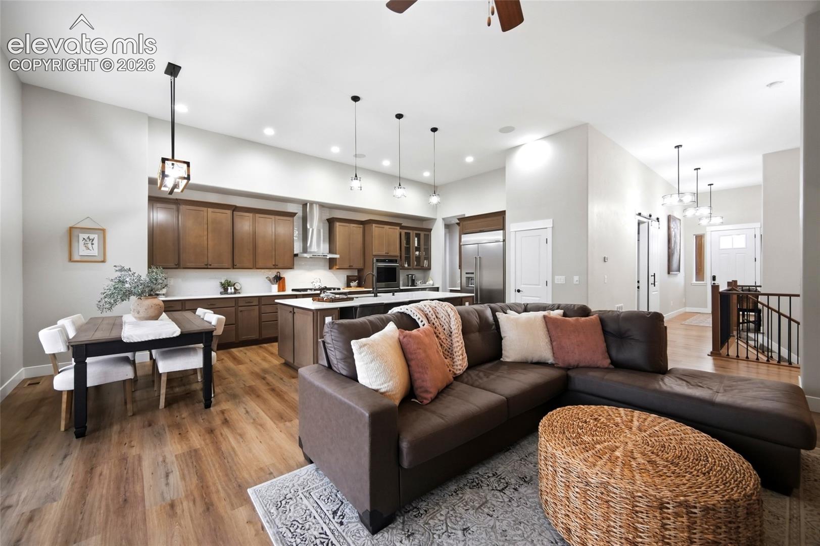Open-concept area featuring wood-finish flooring, recessed lighting, wood cabinetry, a central kitchen island with stone countertops, and stainless steel appliances
