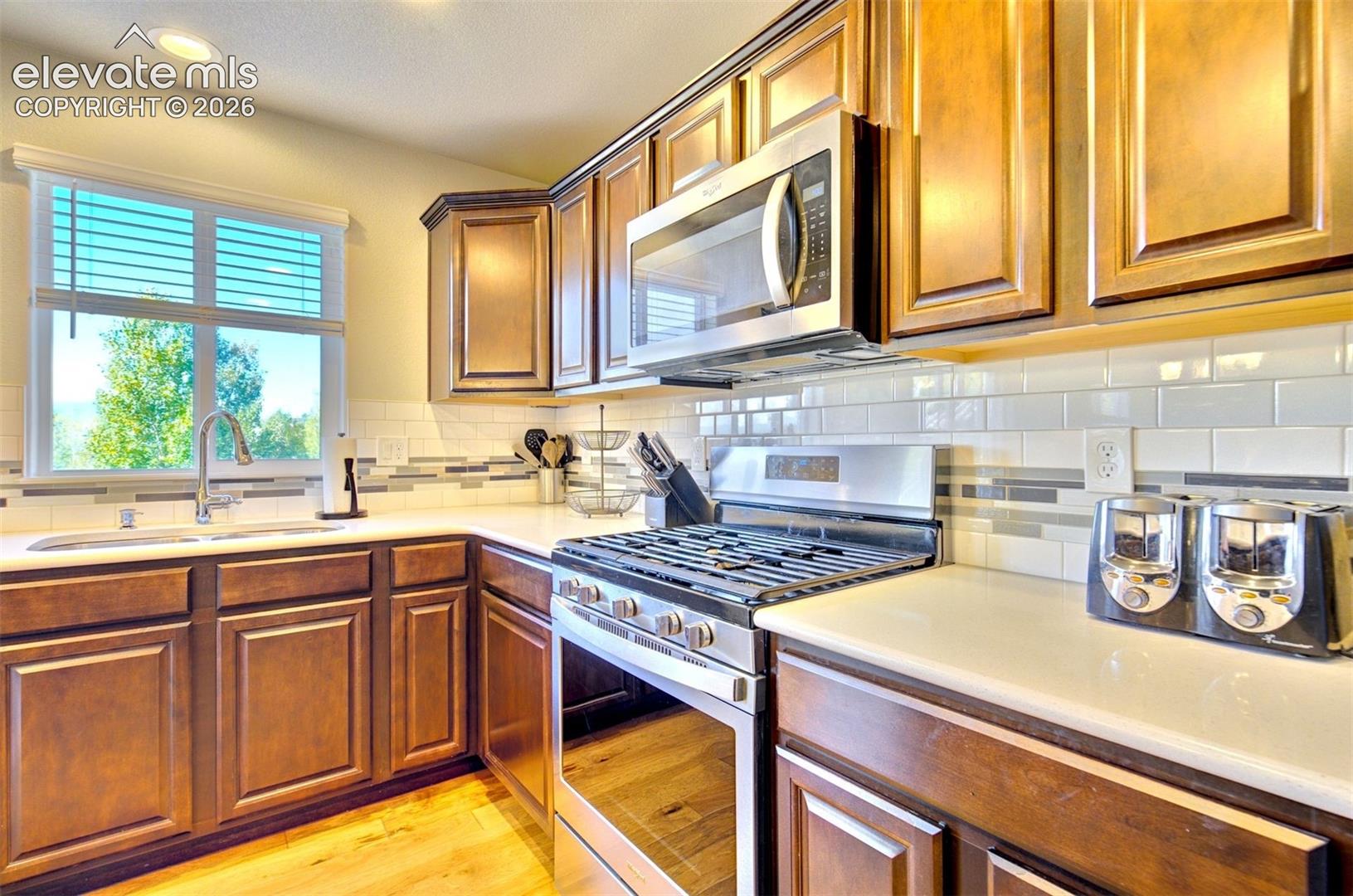 Kitchen featuring stained wood cabinetry, white countertops, subway tile backsplash with decorative stone inlay, stainless steel gas range, and wood-finish flooring