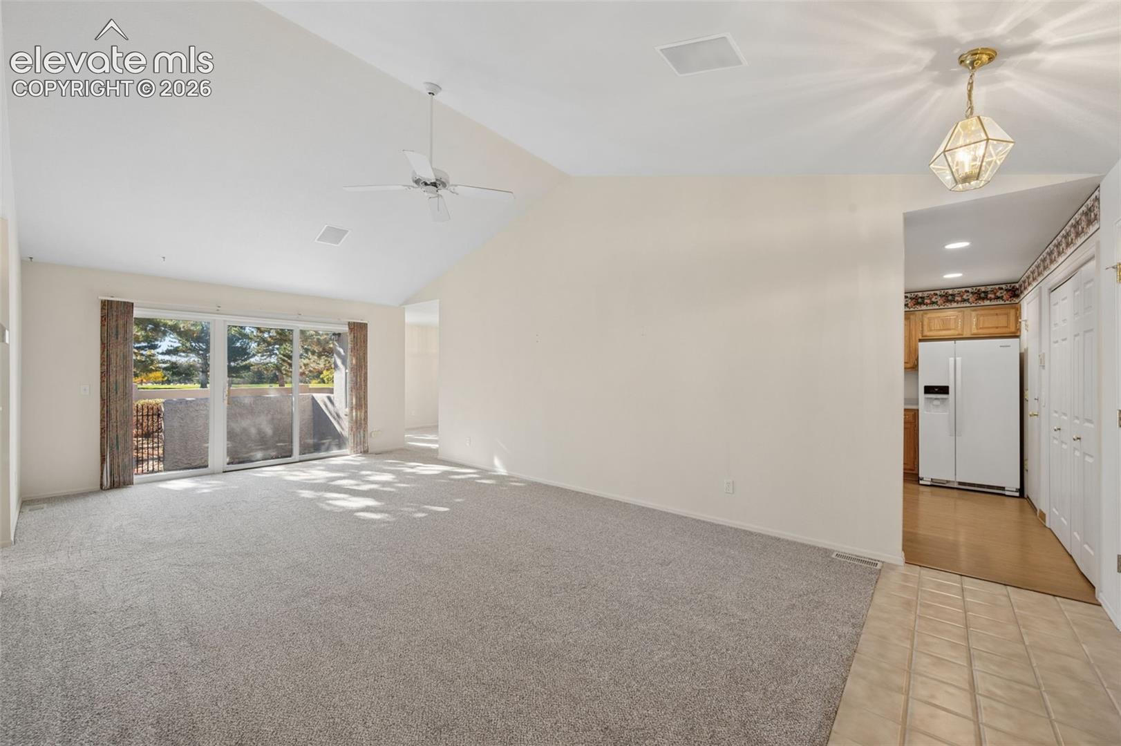 Vaulted ceiling with a white ceiling fan, large sliding glass door, and neutral carpeting
