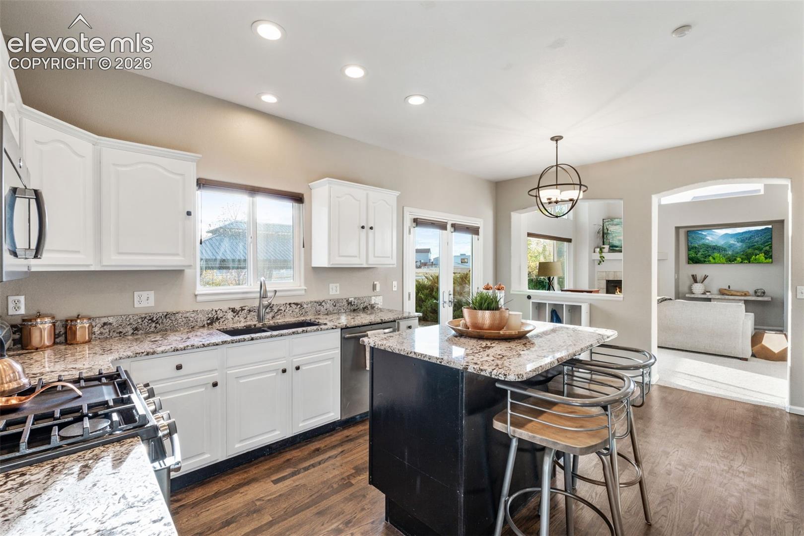 Kitchen featuring white shaker-style cabinetry, stone countertops, a central island with a contrasting dark finish, recessed lighting, and wood-finish flooring