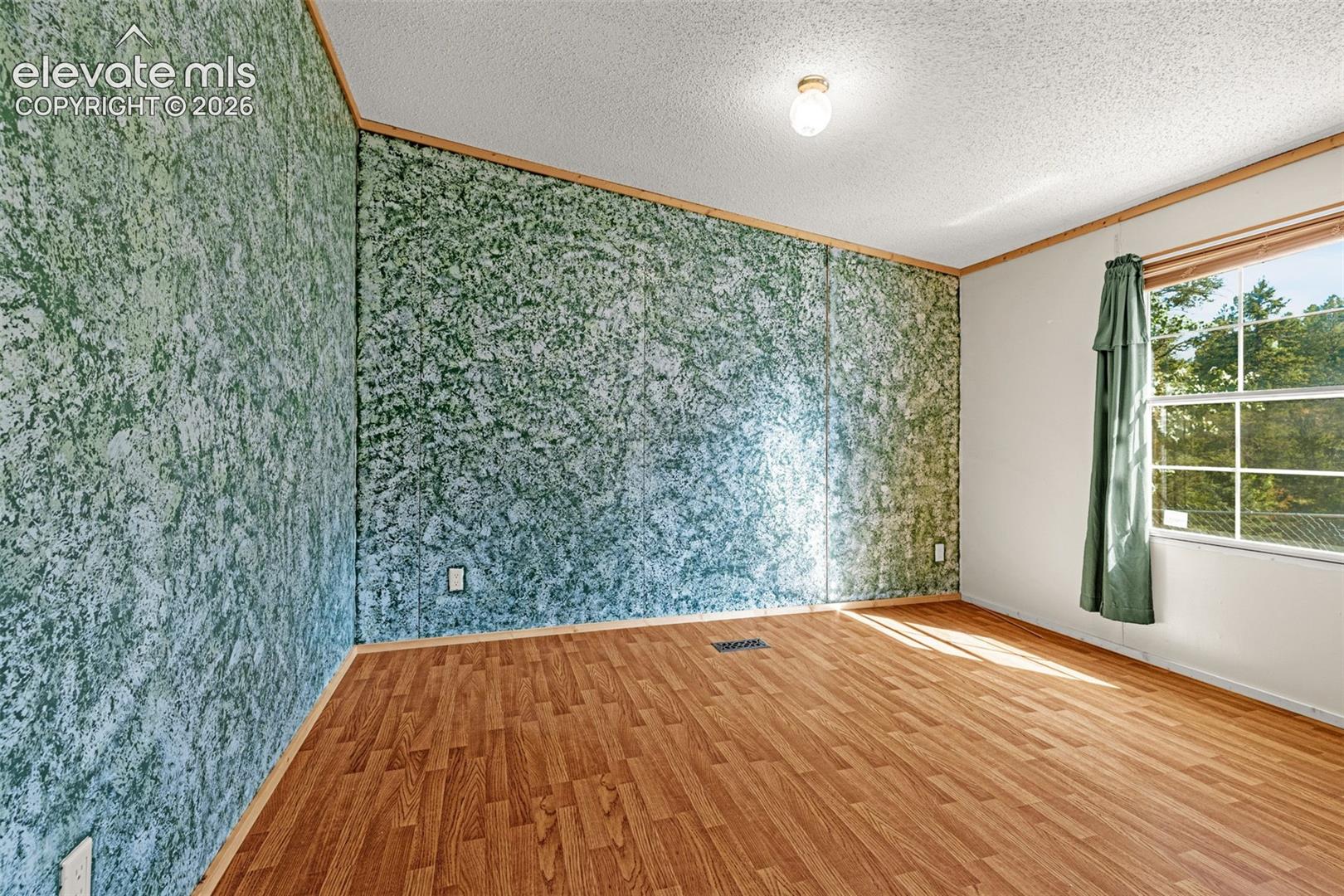 Wood-finish flooring with a textured accent wall and flush-mount ceiling light