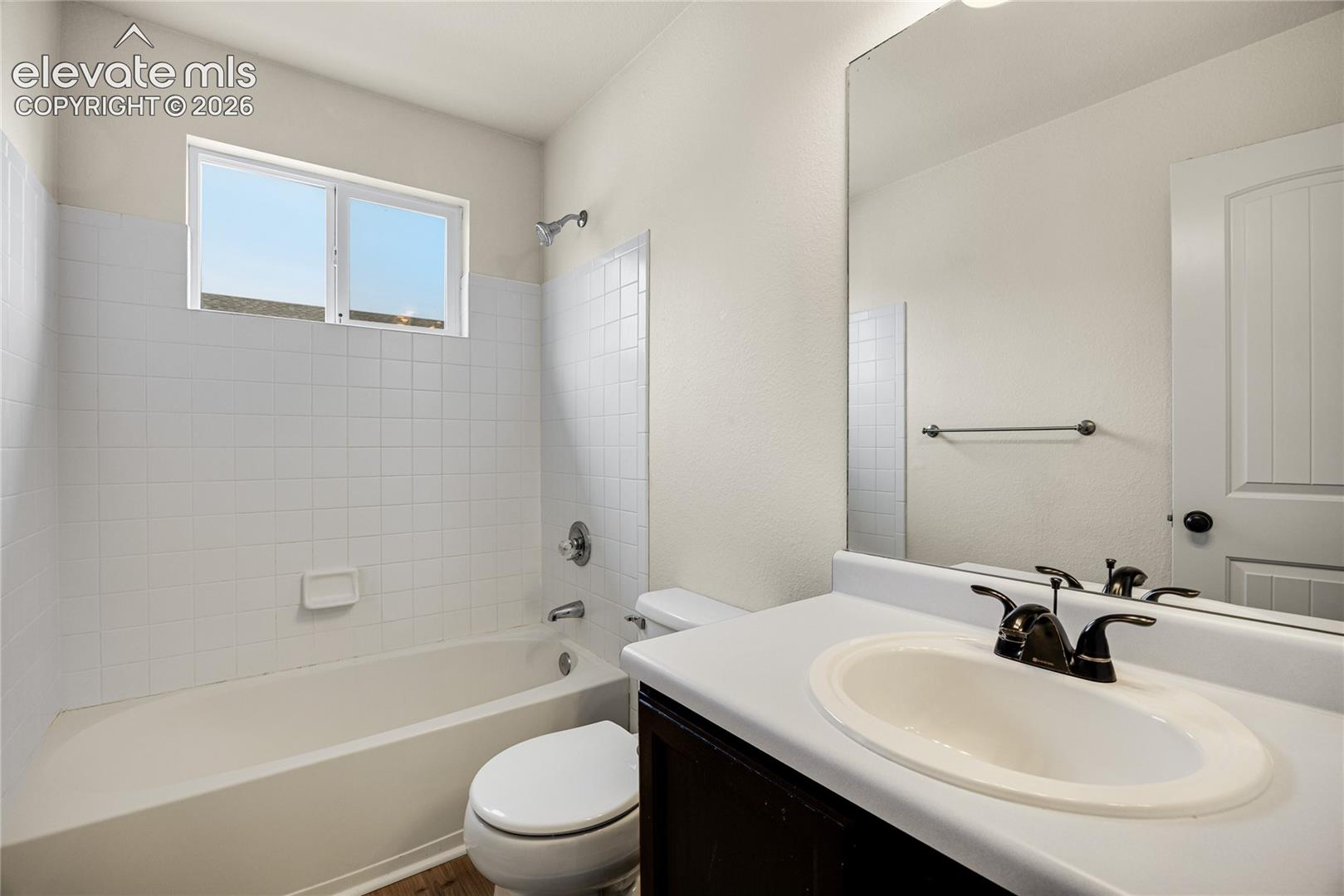 Bathroom featuring a tub-shower combination with white tile surround, vanity with an integrated basin, dark cabinetry, and a full-width wall mirror