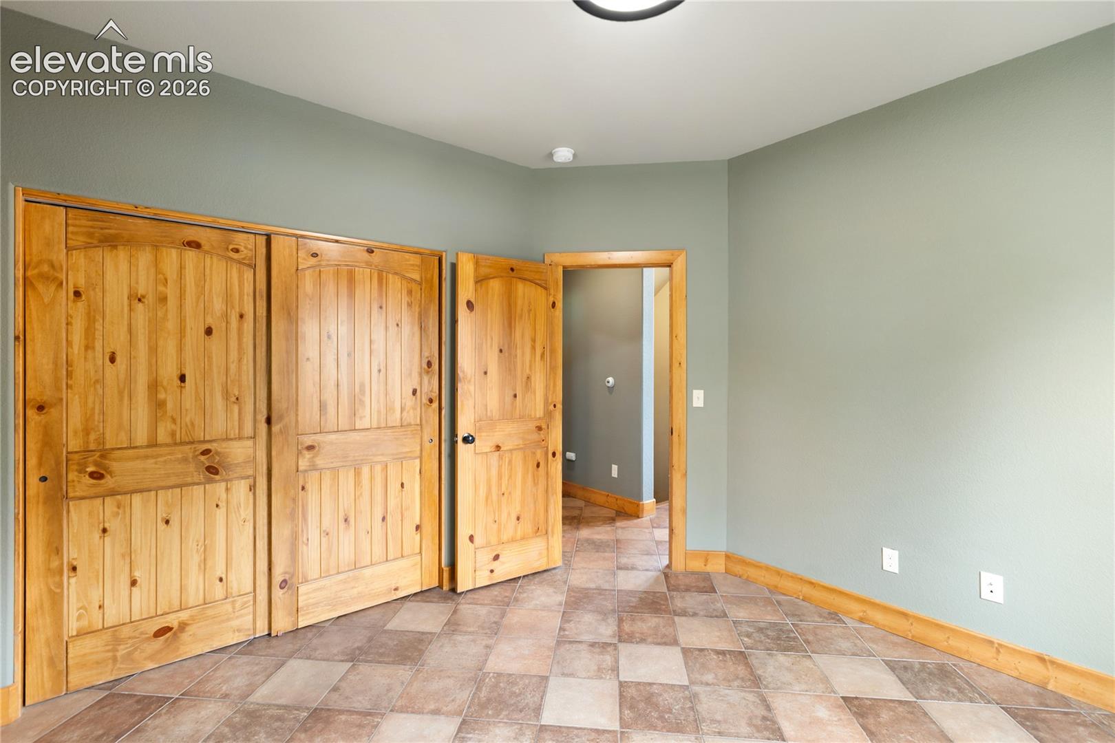 Room featuring natural wood-finish interior doors with arched panel detailing, multi-tonal square tile flooring, and coordinating wood-finish door casings