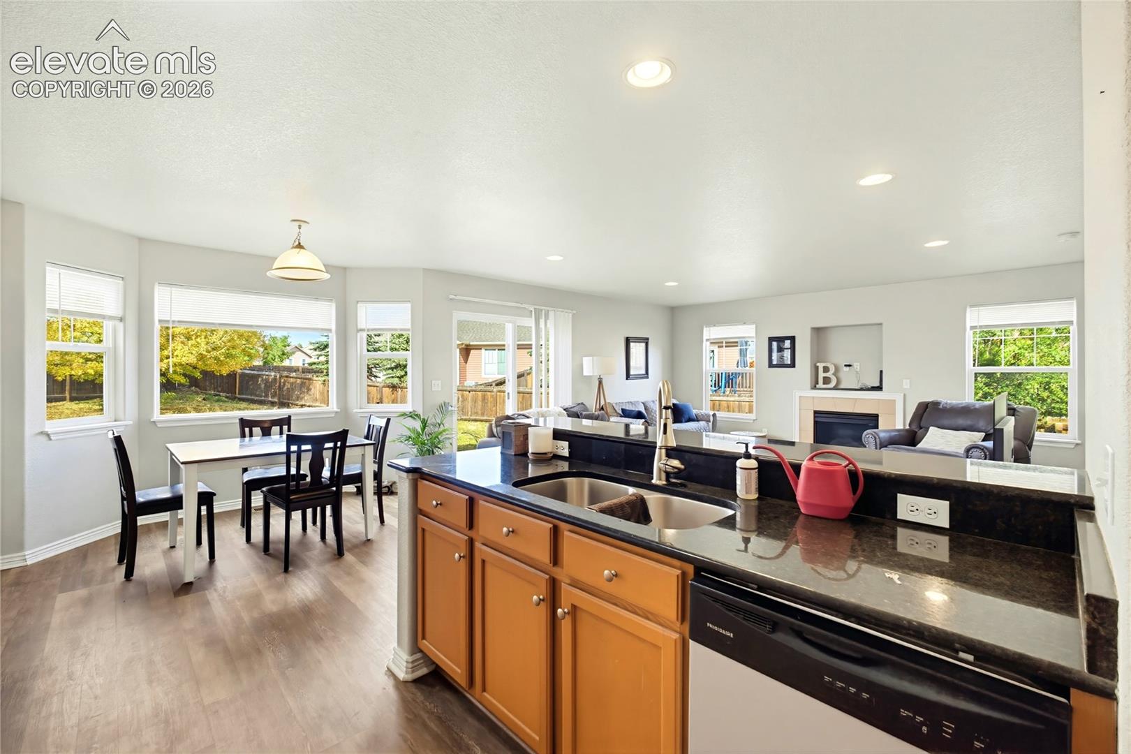 Open-concept kitchen and dining area featuring wood-finish flooring, dark stone-style countertops, recessed lighting, and a neutral color palette