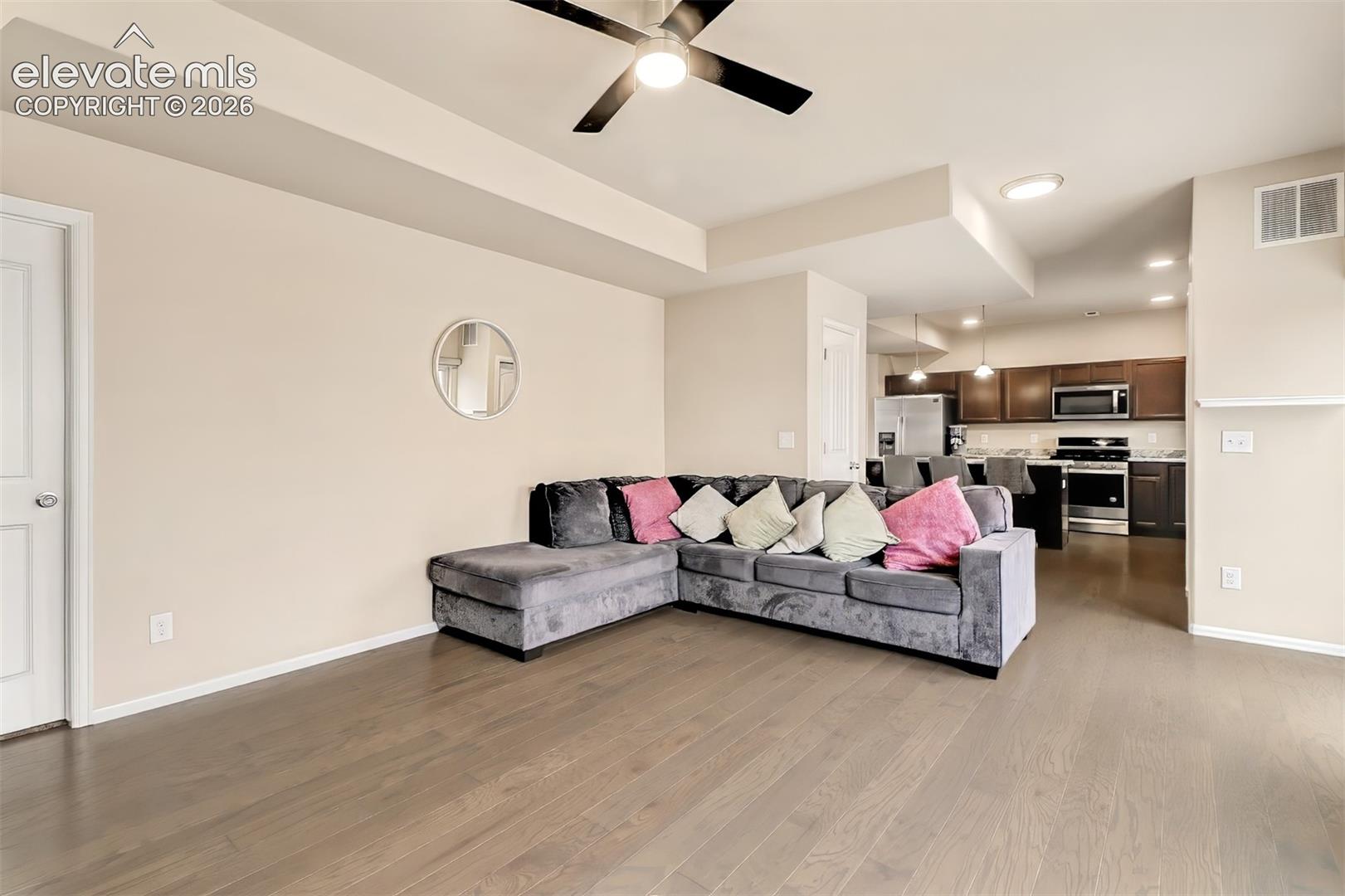 Living area featuring tray ceilings, a ceiling fan with integrated lighting, and wood-finish flooring