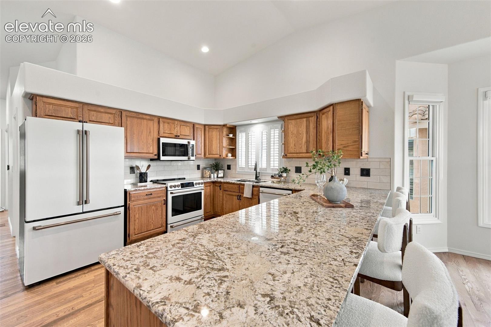 Kitchen featuring wood cabinetry, stone countertops, an expansive breakfast bar, white subway tile backsplash, and wood-finish flooring