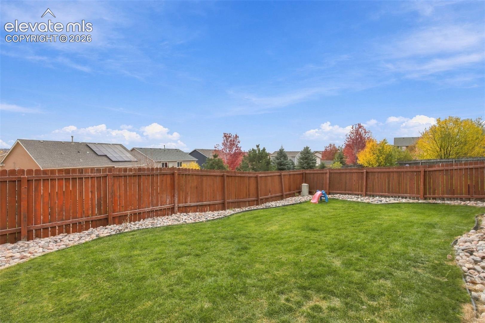 Expansive backyard featuring a manicured lawn, full-perimeter wood privacy fencing, and stone landscape edging