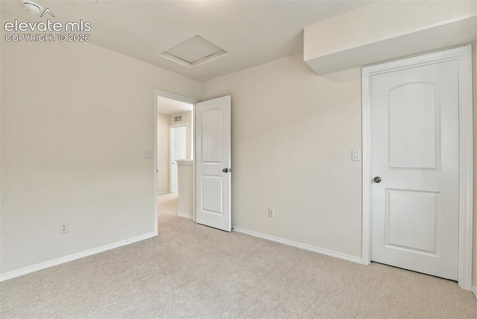 Neutral-toned interior space featuring neutral wall-to-wall carpeting, two-panel arched interior doors, and a ceiling access panel